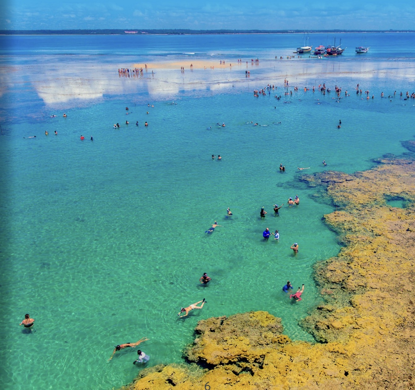 Porto Seguro: vista aérea de banhistas nadando e fazendo snorkel em águas rasas e cristalinas sobre recifes, com barcos ancorados ao fundo