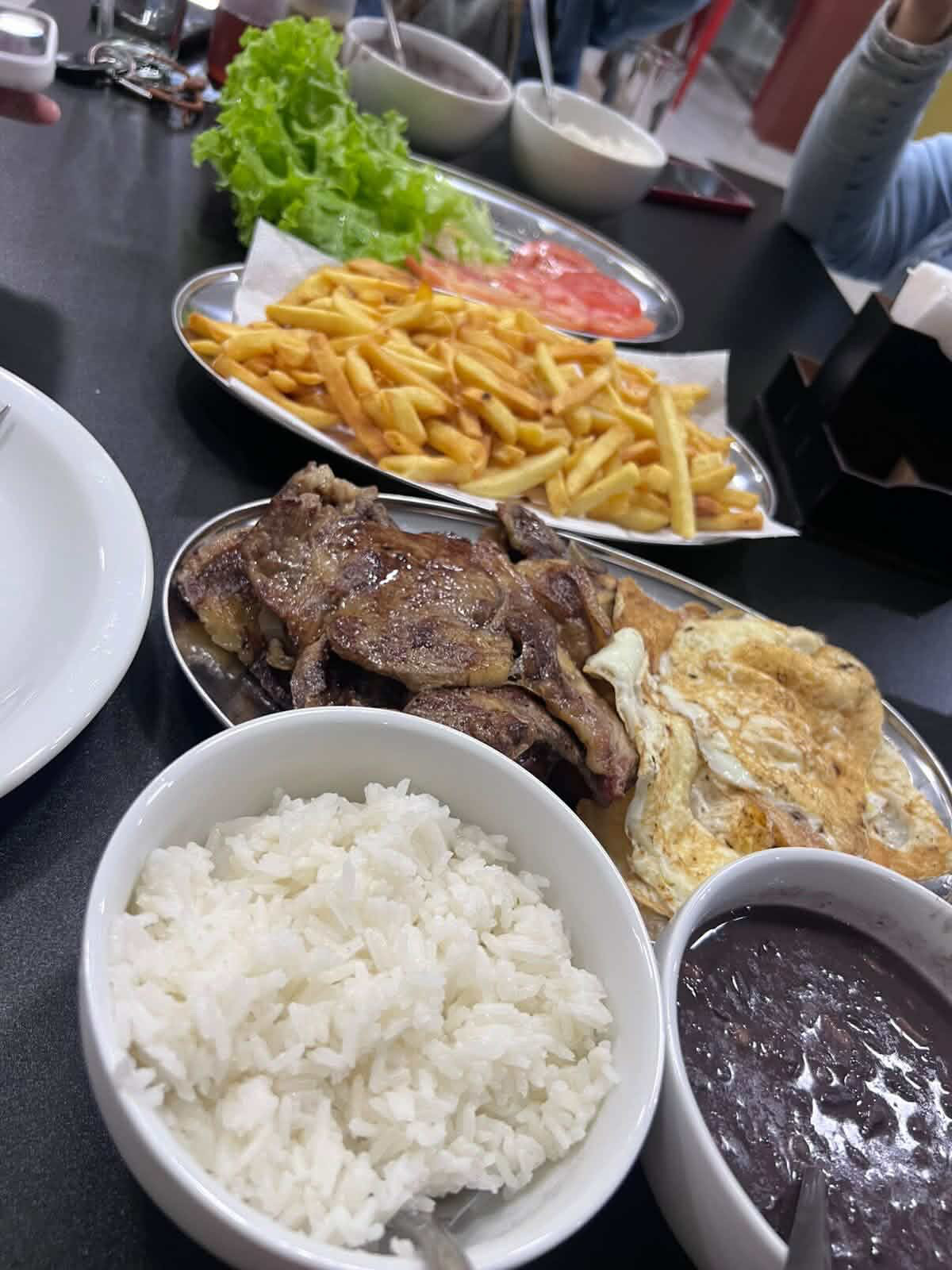 Prato feito com bife, ovo frito, arroz, feijão, fritas e salada na mesa