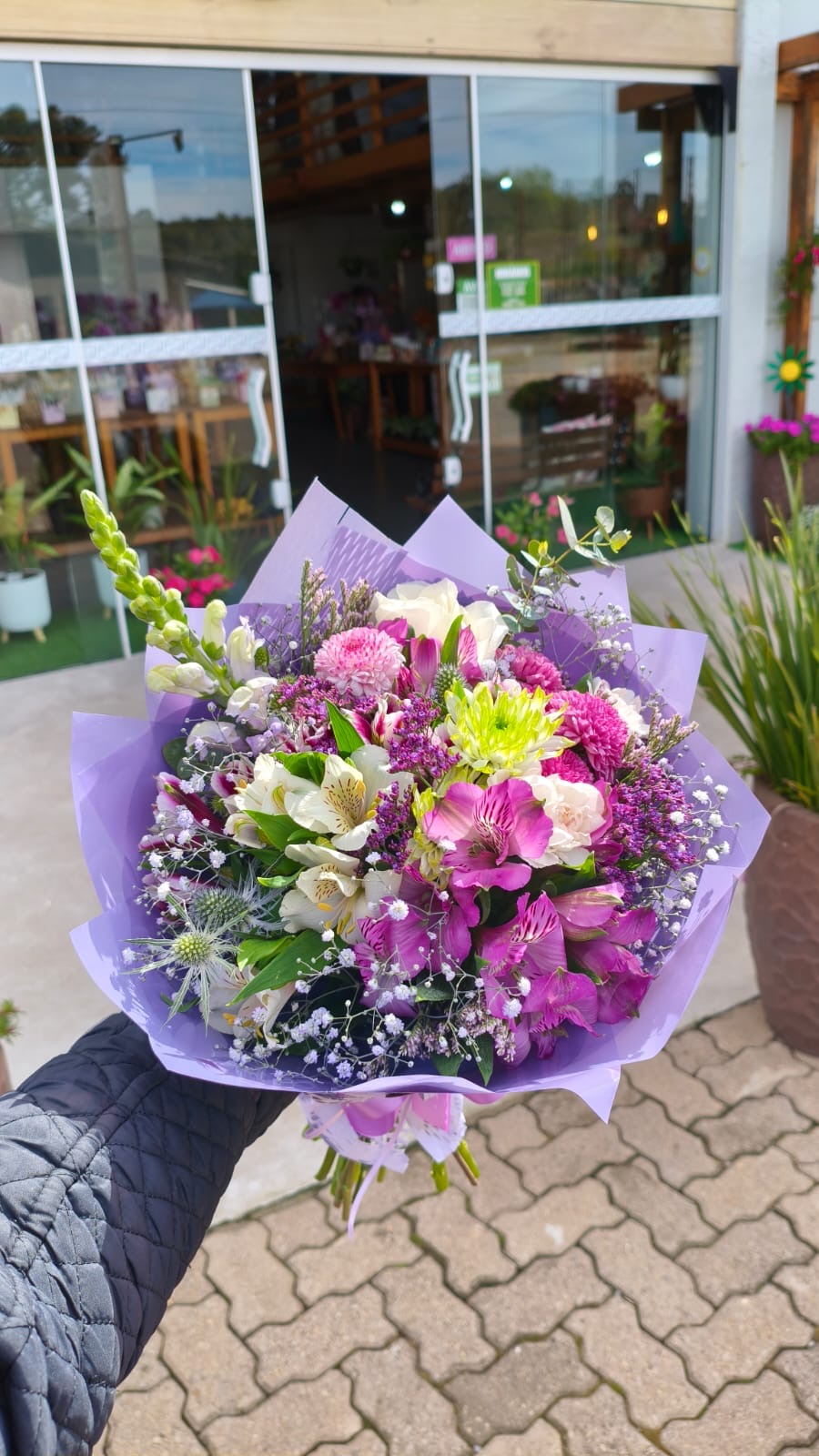 Buquê em tons de rosa, lilás e branco diante da floricultura