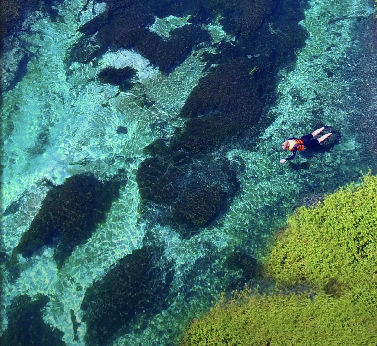 Bonito: vista aérea de pessoa flutuando em rio de águas verde-esmeralda com rochas e vegetação visíveis no fundo