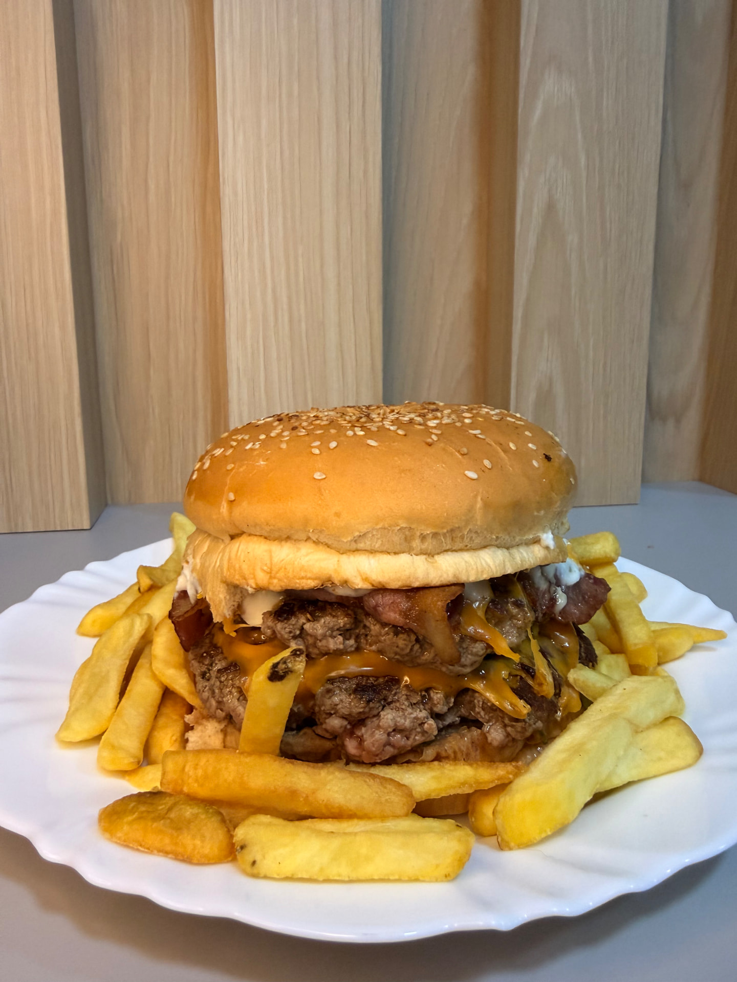 Hambúrguer duplo com cheddar e bacon cercado por batatas fritas no prato