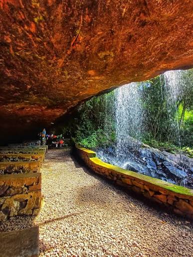 Interior da gruta com bancos de pedra, caminho e cascata ao fundo